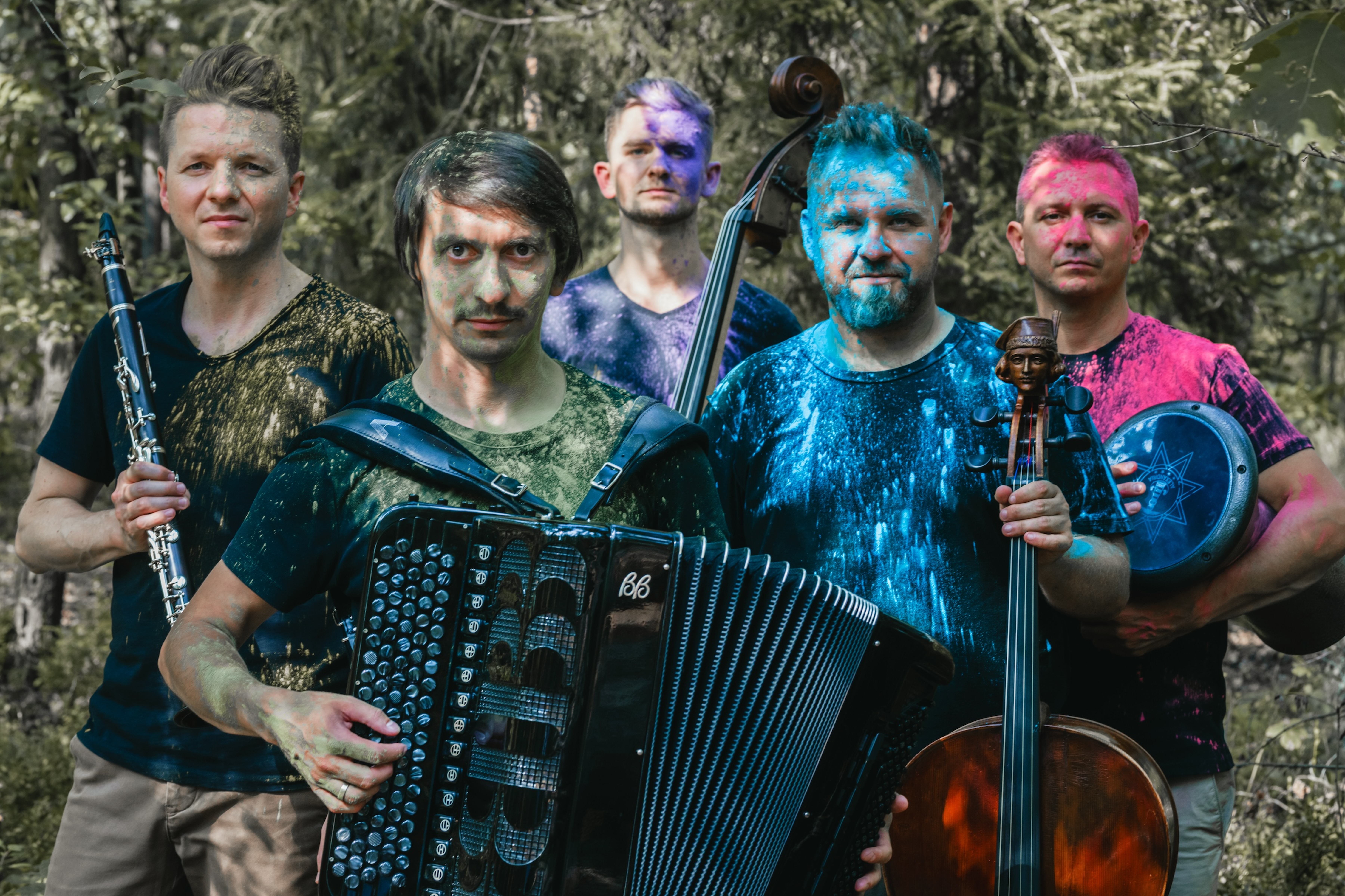 Pięciu muzyków Etnos Ensemble w lesie, ubrania pokryte kolorowymi pigmentami, z instrumentami